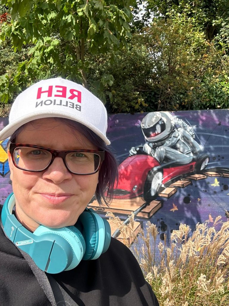 Die Bloggerin steht vor eine Wand, wo ein Astronaut in einer Achterbahn sitzt
