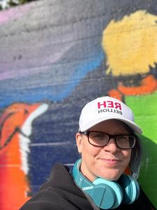 Die Bloggerin lehnt sich an eine bemalte Wand