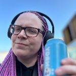 Bloggerin hat Kopfhörer auf und hält in einer Hand die blaue Gönrgy Dose