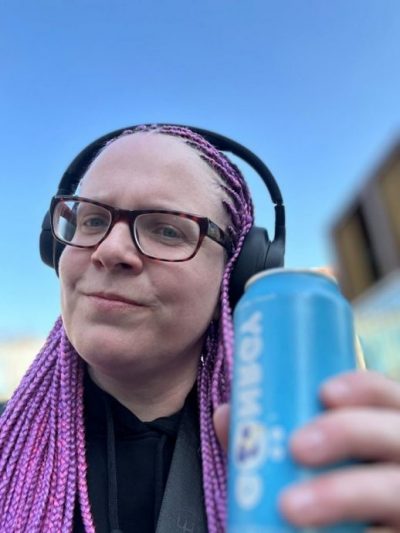 Bloggerin hat Kopfhörer auf und hält in einer Hand die blaue Gönrgy Dose