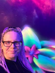 Diee Bloggerin Nena mit lilanen-rosanen Braids steht vor eine bunten gemalten Neonwand